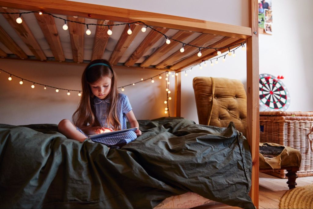 Junges Mädchen, das zu Hause mit einem digitalen Tablet auf einem Bett sitzt.