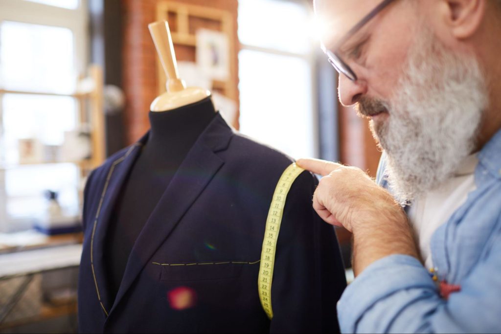 Professioneller Schneider, der ein Maßband verwendet, während er in seiner Werkstatt eine Jacke ändert.