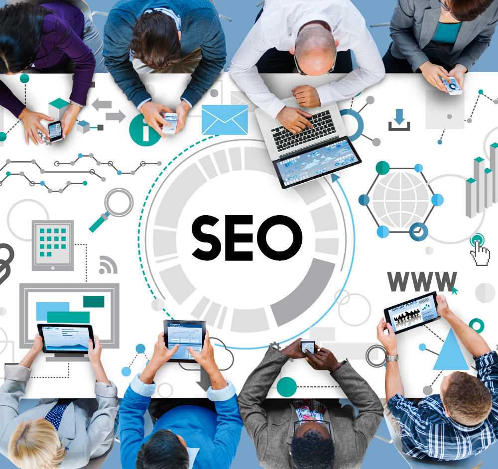 กลุ่มคนที่ถืออุปกรณ์ต่าง ๆ บนโต๊ะพร้อมเขียน "SEO" ไว้