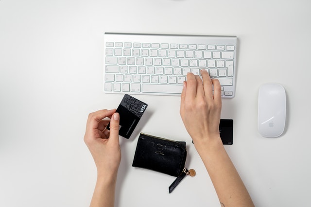 mão segurando um cartão de crédito enquanto digita em um teclado
