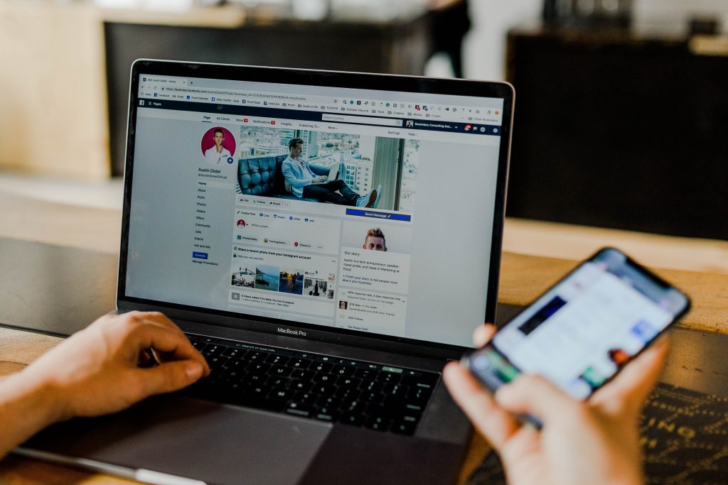 Écran d'ordinateur portable avec profil Facebook, tenant le téléphone à la main