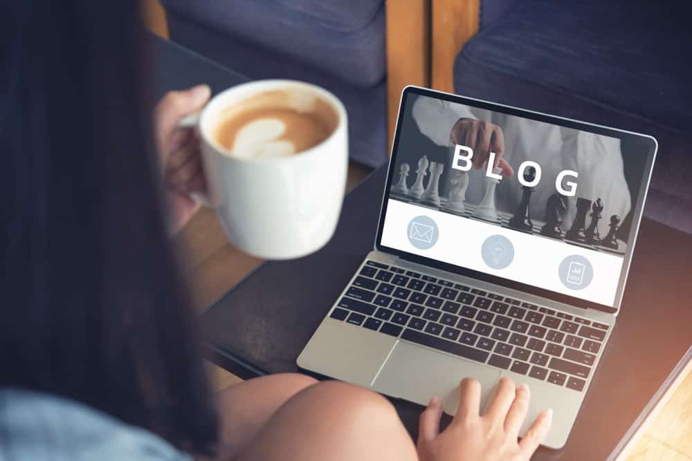 Femme ouvrant un site de blog sur son ordinateur portable tout en tenant une tasse de café.