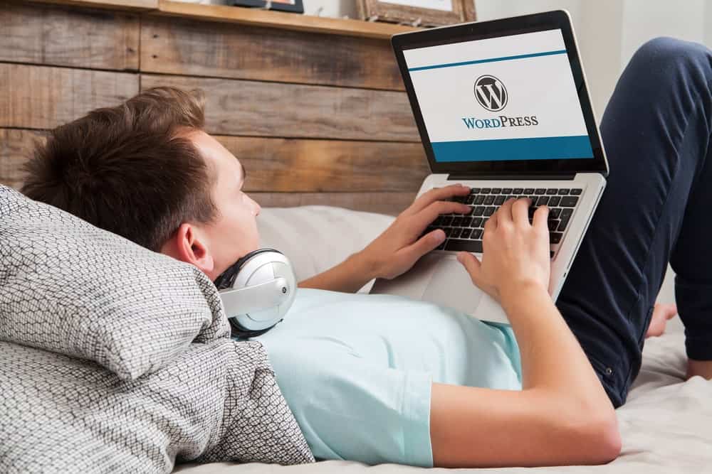 Homme allongé sur son lit lors de l'ouverture de WordPress sur son ordinateur portable.
