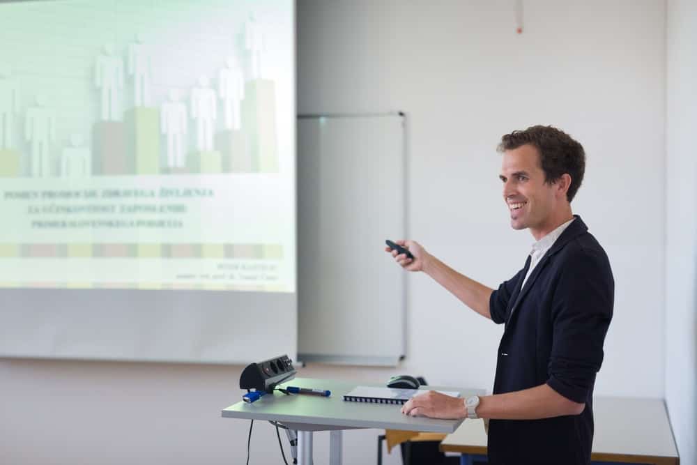 Un uomo con un clicker powerpoint lo punta sullo schermo del proiettore mentre si presenta durante la riunione.