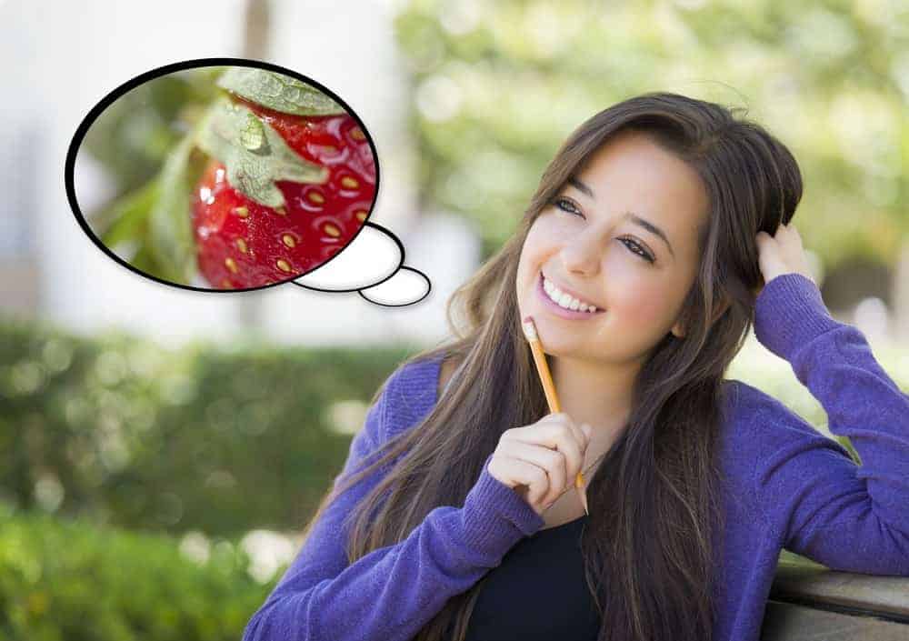 Donna pensante con una matita sul mento e una testa a bolle sul lato con foto di fragola.