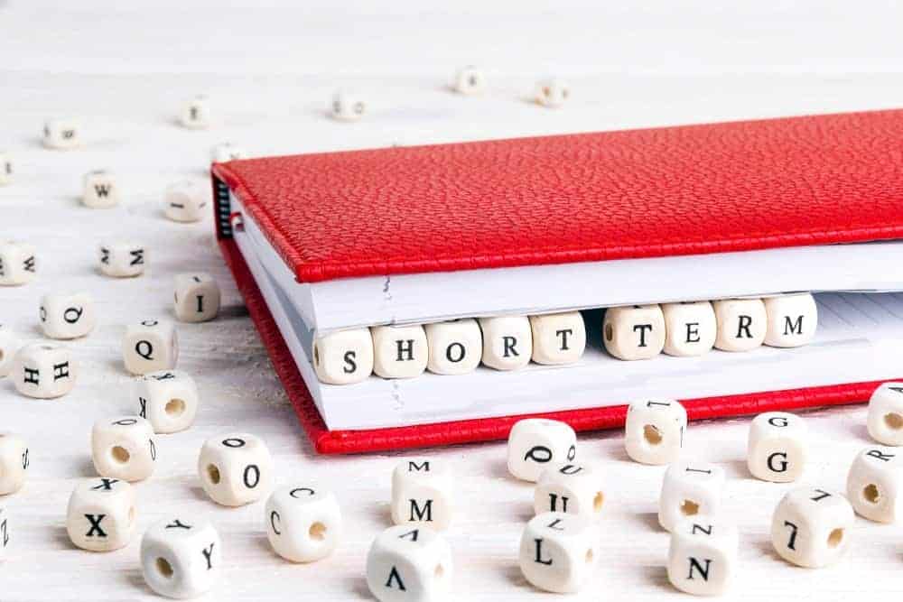 Le parole "Short Term" scritte a dadi da scarabeo tra le pagine di un taccuino rosso.