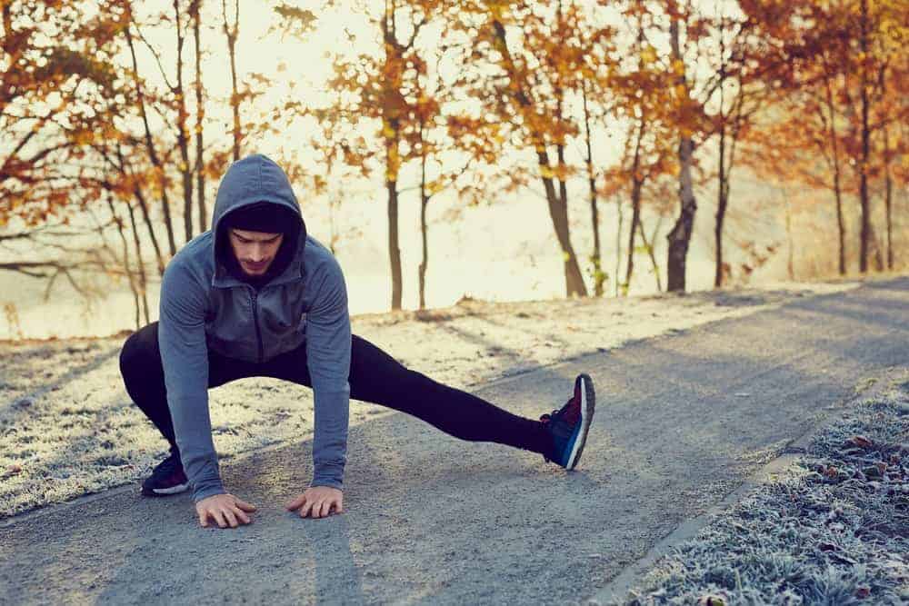 Un uomo che indossa una giacca con cappuccio facendo uno stretching all'aperto.