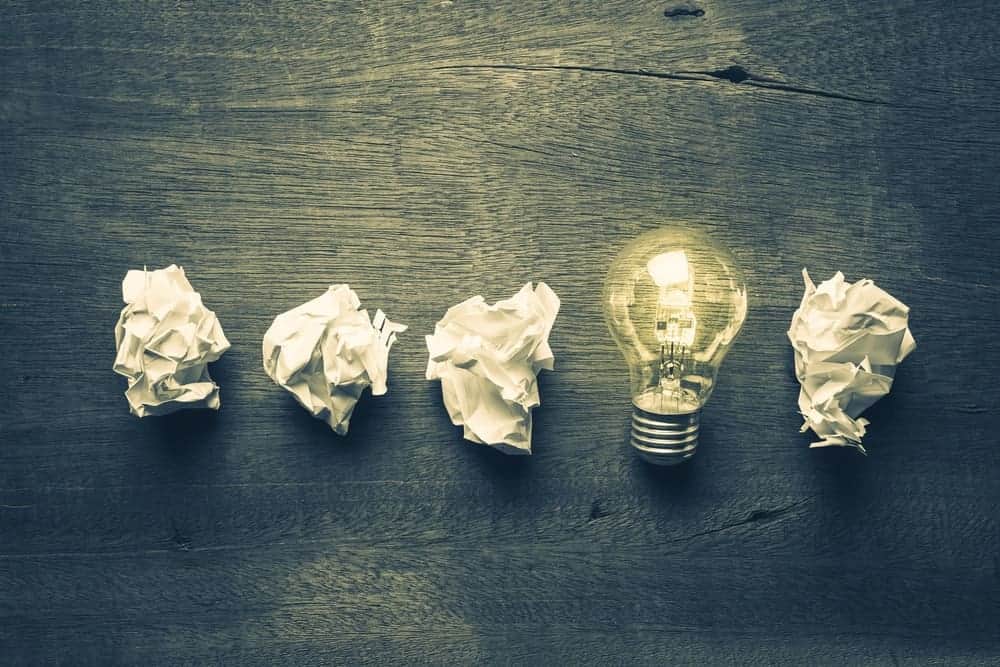 Una lampadina accesa circondata da carta bianca stropicciata in una forma lineare su una scrivania in legno.