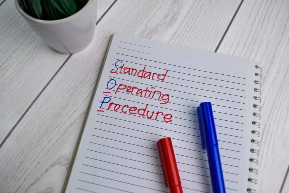 Procedura de operare standard scrisă pe un caiet peste o masă din scânduri de lemn.