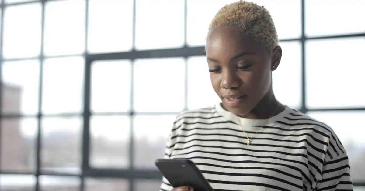 Femme en chemise à col rond à rayures blanches et noires tenant un smartphone noir