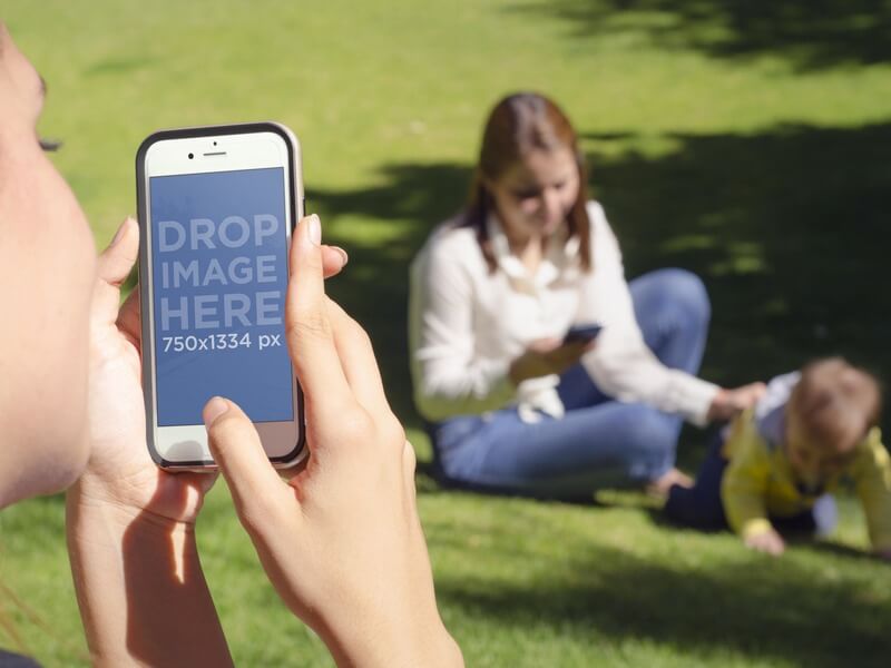 iPhone Mockup لفتاة تلتقط صورة لصديق وطفل في الحديقة