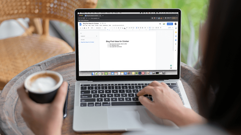 Machetă care prezintă o femeie care lucrează la un Macbook și bea cafea