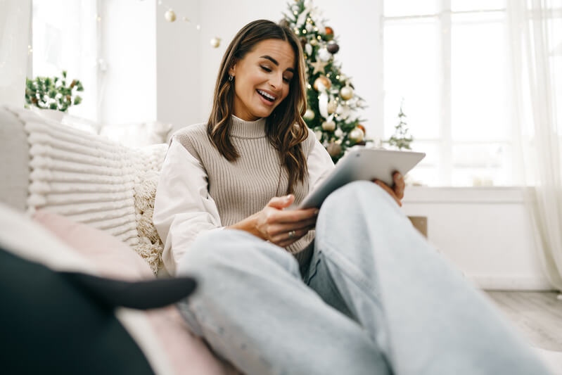 Femeie frumoasă care se relaxează pe canapea cu tabletă digitală de Crăciun