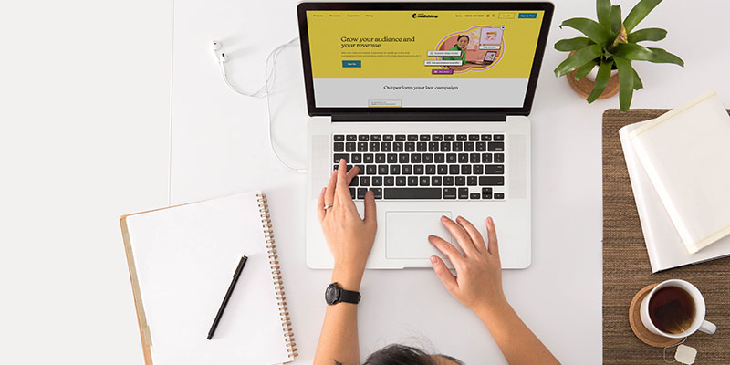 Orang mengetik di laptop dengan buku catatan dan pena di sampingnya