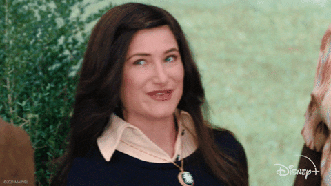 gif TV. De la WandaVision: Agnes Harkness (Kathryn Hahn) ne face cu ochiul exagerat și își înclină capul cu un zâmbet.