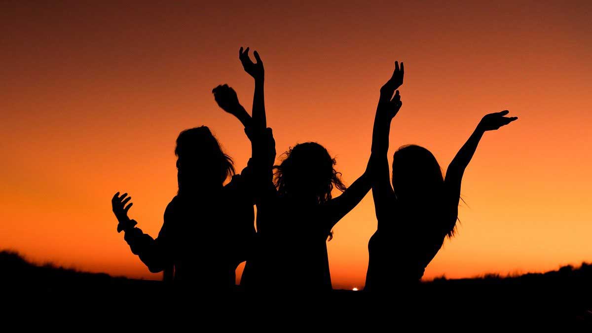 silueta de 3 mujeres felices contra el cielo naranja.