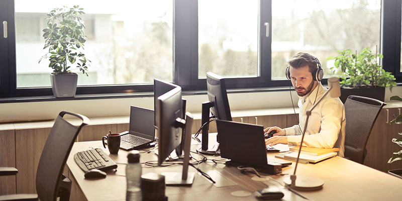 Bărbat cu căști cu fața la ecranul computerului