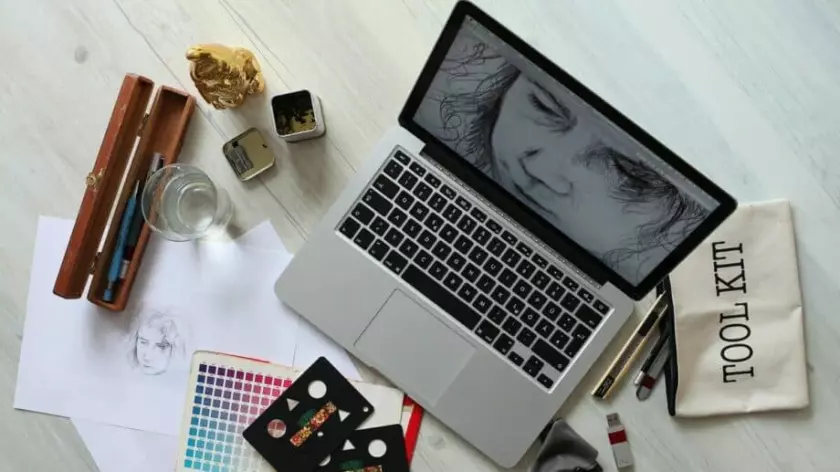 Un ordinateur portable posé sur une table à côté de fournitures artistiques est prêt à trouver des conseils de croissance commerciale pour les artistes.