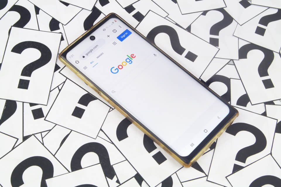 Мобильный телефон на главной странице Google в окружении вопросительных знаков
