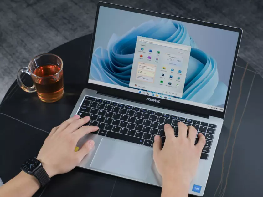 Une personne utilisant un ordinateur portable ACEMAGIC AX15 sur une table avec une tasse de café.