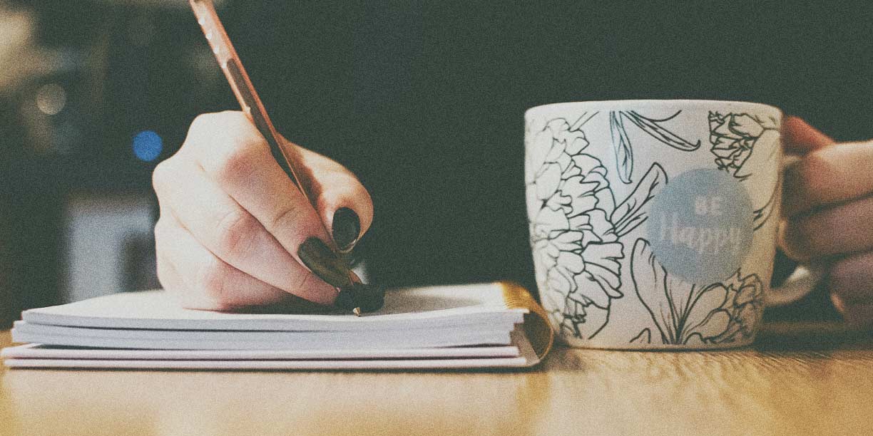 Persoană care scrie într-un caiet cu o ceașcă de cafea pe masă