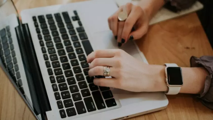 Kobieta pisząca na laptopie z zegarkiem Apple.