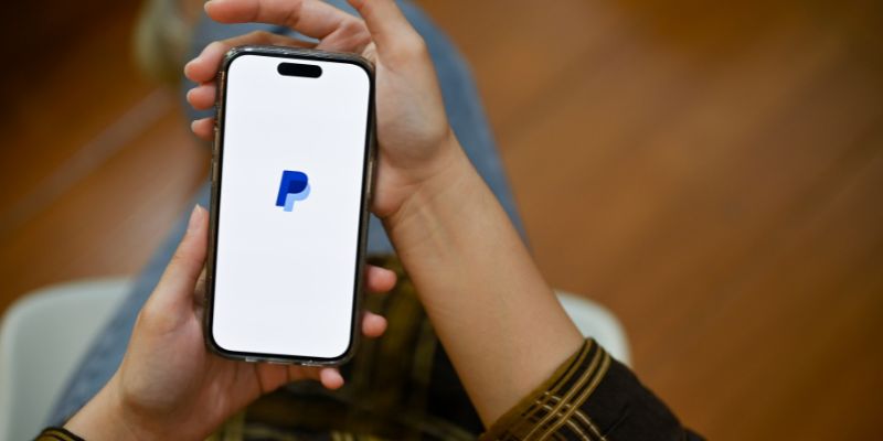 tangan memegang smartphone dengan logo paypal