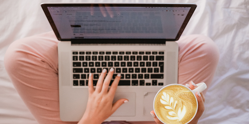 Una mujer escribiendo en su computadora portátil mientras toma café